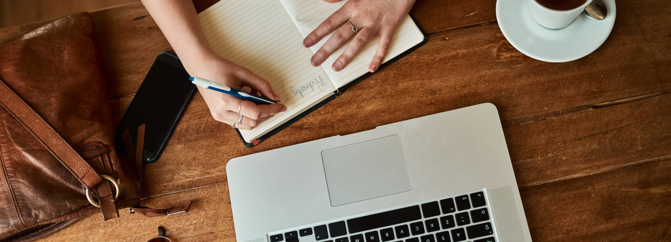 A woman at computer with coffee and notebook