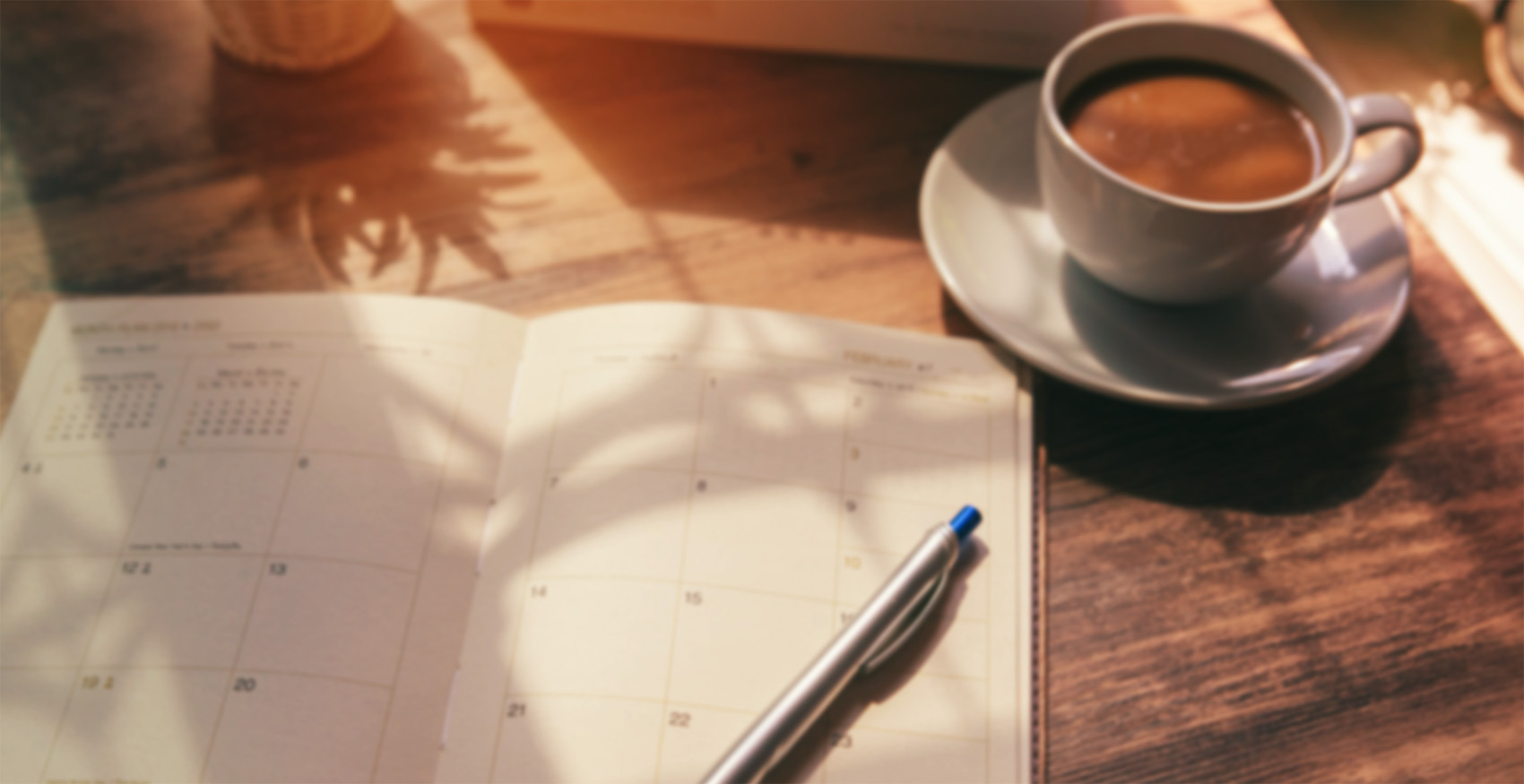 Calendar planner laying open next to cup of coffee
